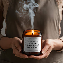 Load image into Gallery viewer, CLASSY SASSY AND A BIT BAD ASSY FUNNY SCENTED CANDLE IN AMBER JAR BEING HELD