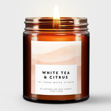 Load image into Gallery viewer, Scented candle in an amber jar labeled 'White Tea & Citrus' by Terra Mater Studio on a light gray background.
